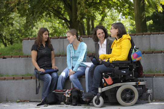 Vier Studierende, darunter Studierende mit Behinderung, sitzen gemeinsam auf dem Campus.